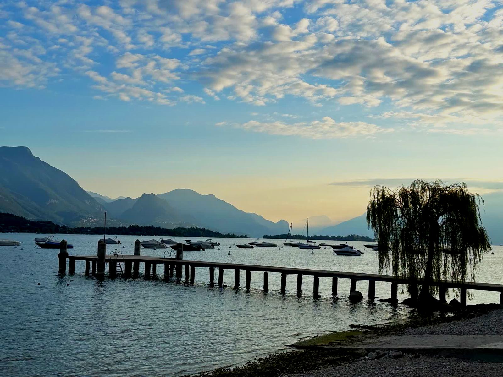 A jetty at Lake Garda in the evening, boats moored and mountains behind.